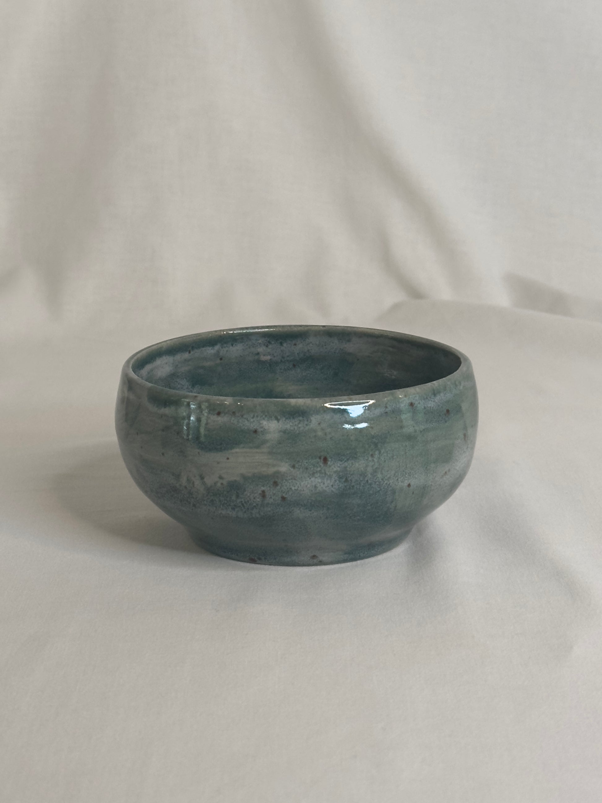 Bol artisanal en céramique émaillée vert foncé, avec des nuances de gris et des détails mouchetés. Idéal pour les petits déjeunés, soupes, salades ou autres plats, il ajoute une touche élégante et naturelle à la table.